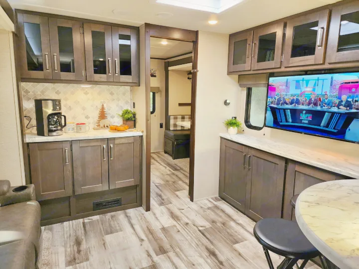 Spacious rv rental interior: kitchen with coffee maker, living area with TV, and dining booth in background.. Grand Design Transend Xplor 315BH 2023