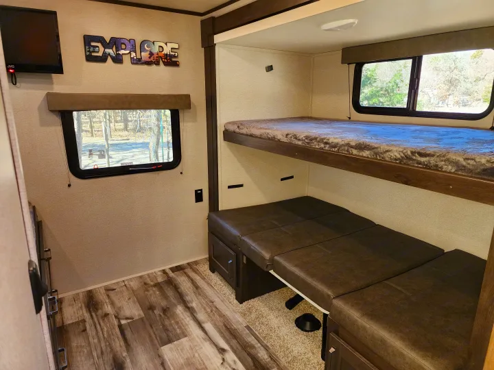 This inviting RV rental interior showcases a cozy bunk bed, convertible seating, and a TV, ideal for family trips.. Grand Design Transend Xplor 315BH 2023