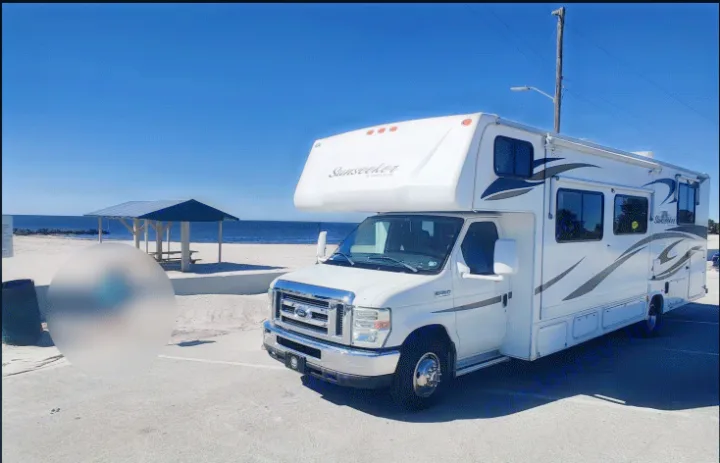 White Sunseeker RV rental parked by a sunny beach with a picnic shelter and clear blue sky. Ready for your coastal adventure!. Forest River Sunseeker 2012