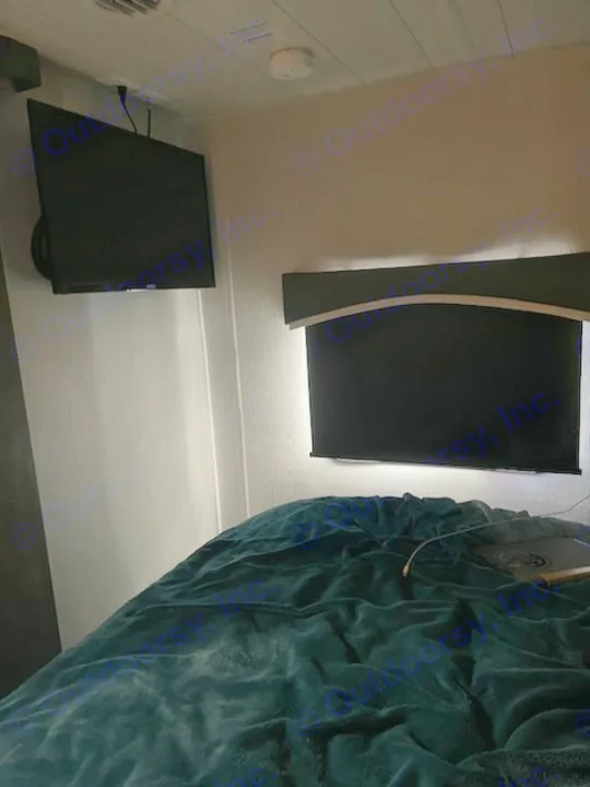 Comfortable RV rental bedroom with two wall-mounted TVs, a soft blanket, and subtle lighting creating a cozy ambiance.. Forest River Evo 2022