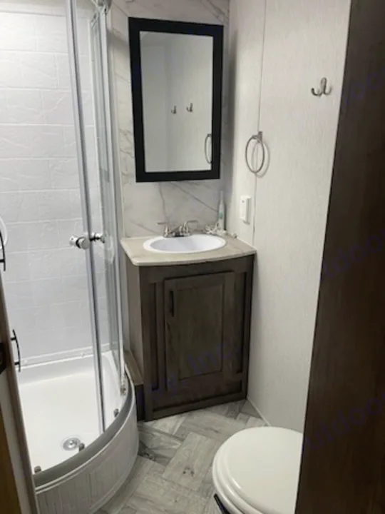 This RV rental features a modern, compact bathroom with a curved glass shower, sink vanity, and toilet.. Forest River Evo 2022