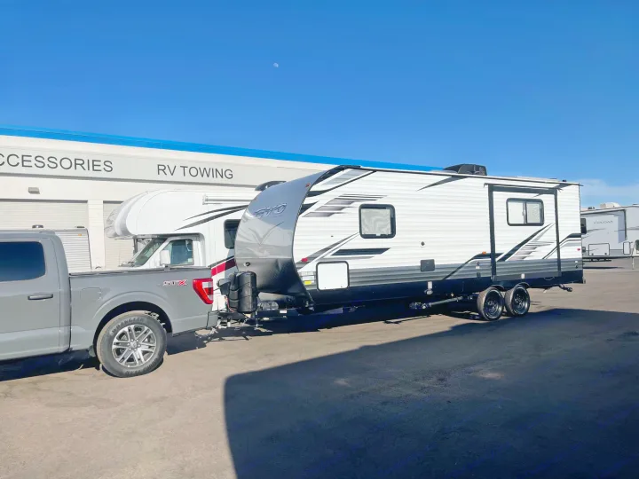 Grey pickup tows white/black EVO travel trailer RV at an RV towing/accessories center, great for rv rental.. Forest River Evo 2022