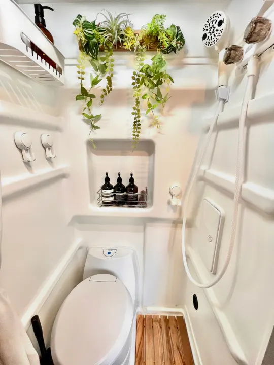 Compact RV rental bathroom features a modern toilet, shower, Aesop toiletries, and decorative plants, optimizing small space comfort.. Winnebago Solis 2022