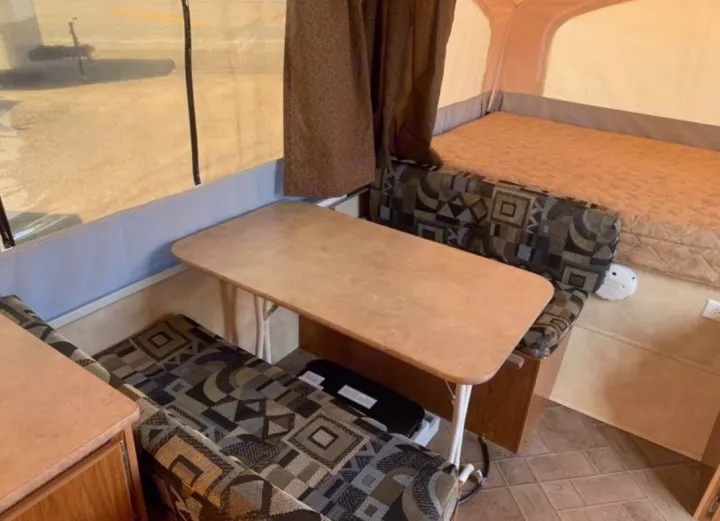 Cozy RV rental interior of a pop-up camper: a dinette with patterned bench seating, table, and bed.. Coachmen Clipper 2008