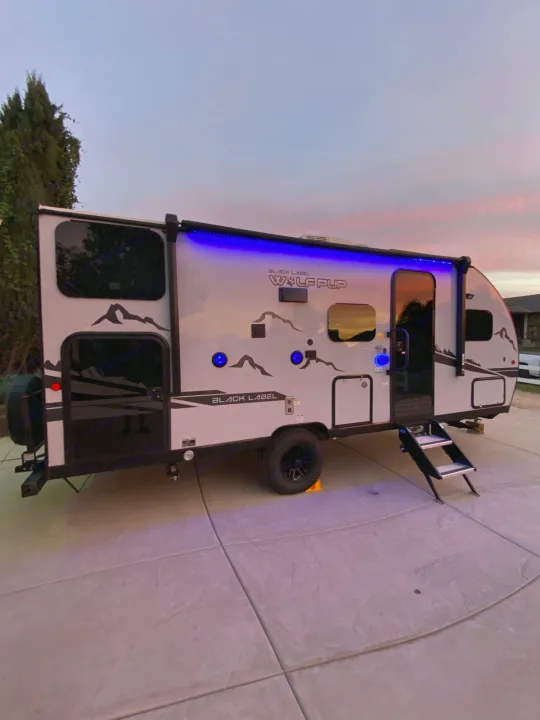 Experience comfort: This sleek Cherokee Wolf Pup Black Label RV rental shines under twilight with cool blue lights, ready for adventure.. Forest River Cherokee Wolf Pup 2022