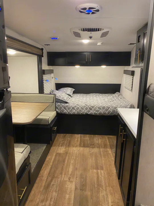 Modern RV rental interior showing a comfortable bed, dinette, storage cabinets, and wood-look flooring.. Forest River Cherokee Wolf Pup 2022