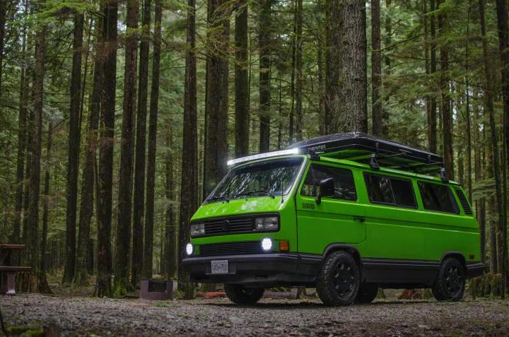 Vibrant green 2WD VW Vanagon with a rooftop tent parked in a dense forest. Explore nature with this RV rental.. Volkswagen Vanagon 1989