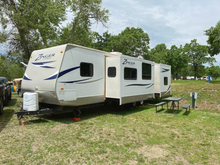 White Zinger travel trailer RV rental parked at a grassy campsite with slide-outs extended and a picnic table.. Crossroads RV Zinger 2013