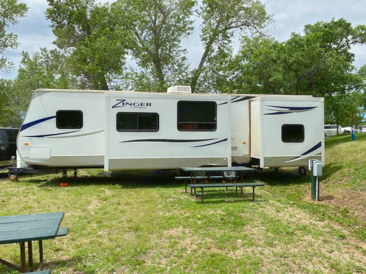 Your next RV rental awaits: a white Zinger travel trailer fully set up at a green campsite.. Crossroads RV Zinger 2013