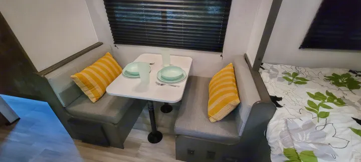 Cozy RV rental interior featuring a dinette with a set table, striped pillows, and a nearby bed with patterned bedding.. Heartland RVs Mallard 2022