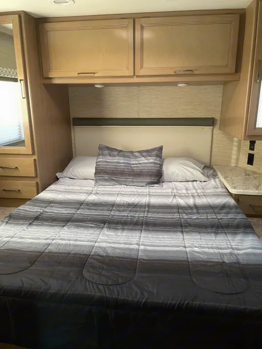 Cozy RV rental bedroom featuring a striped comforter, overhead cabinets, and compact built-in storage.. Thor Coleman 2022
