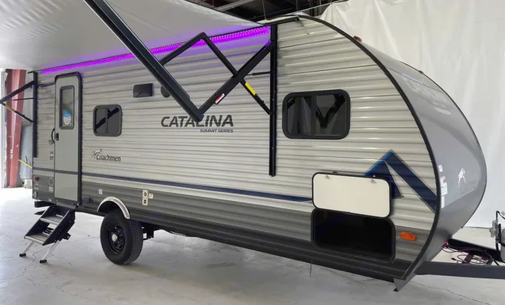 Modern light grey travel trailer with purple-lit awning, steps, and storage, ideal for your next rv rental adventure.. Coachmen Catalina 2022