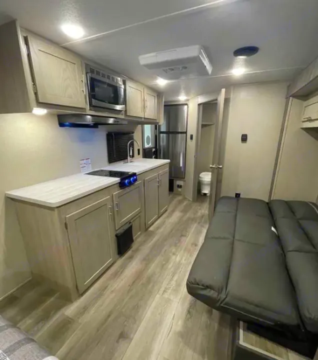 Inside an RV rental: a well-equipped kitchen with stove & microwave, comfortable sofa, full-size fridge, & bathroom.. Coachmen Catalina 2022