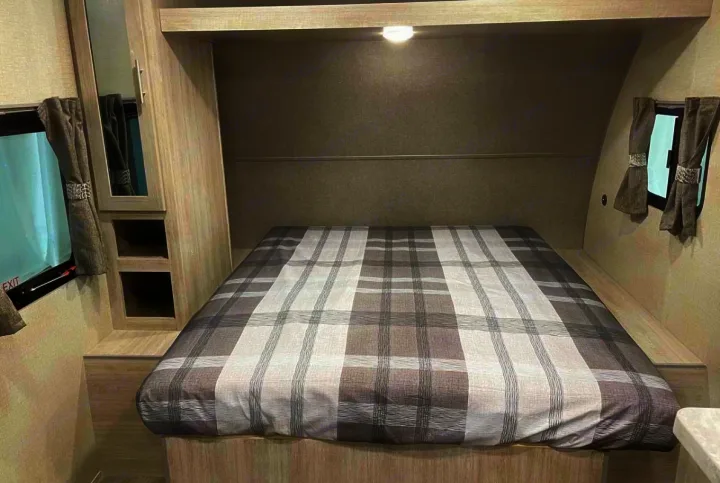 RV rental bedroom interior, showcasing a cozy plaid bed, built-in storage, and curtained windows.. Coachmen Catalina 2022