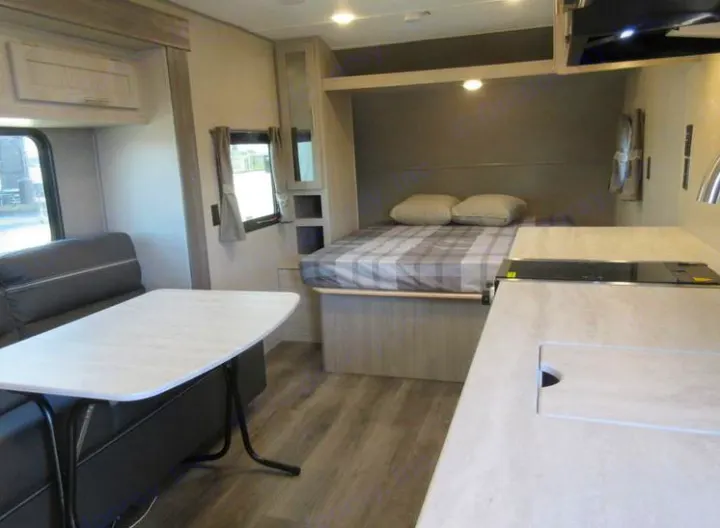 Inside an RV rental: Compact living space featuring a cozy bed, dining area with table, and compact kitchen.. Coachmen Catalina 2022