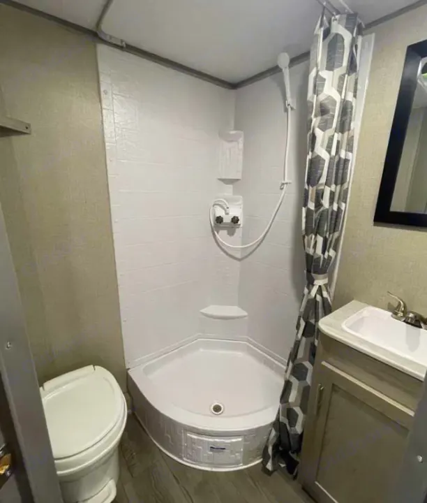 Compact RV rental bathroom featuring a corner shower with patterned curtain, toilet, and vanity with sink.. Coachmen Catalina 2022