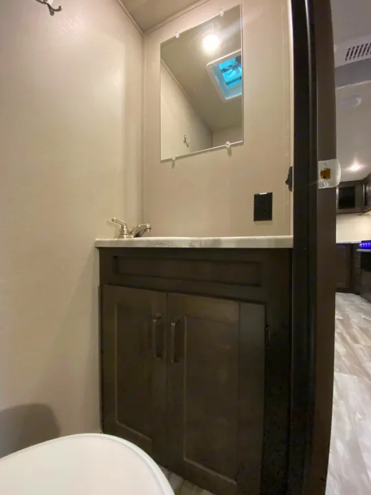 Compact RV rental bathroom with dark vanity, mirror, sink faucet, and partial toilet. Bright and functional interior.. Grand Design Transcend Xplor 2022