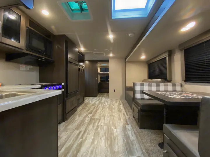 Bright RV rental interior featuring a modern kitchen, booth dinette, and living area, with wood-look flooring.. Grand Design Transcend Xplor 2022