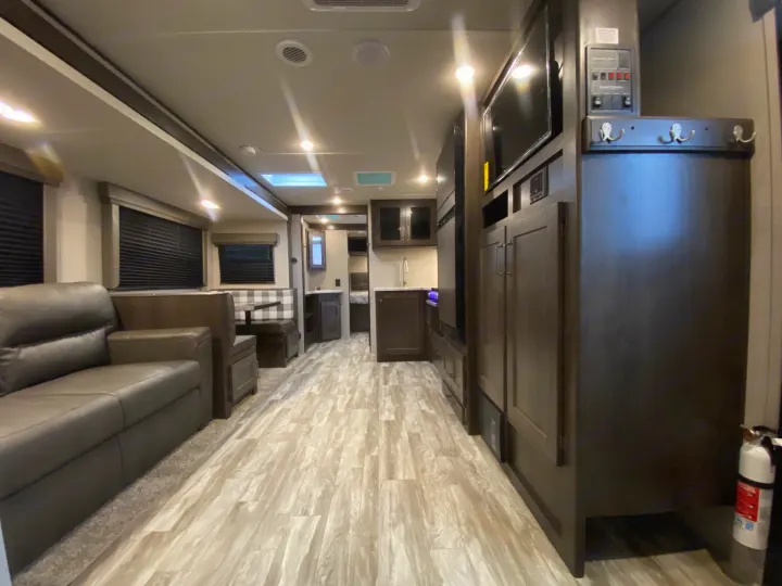 Spacious, modern RV rental interior with living area, kitchen, dinette, and bright lighting. Fire extinguisher visible.. Grand Design Transcend Xplor 2022