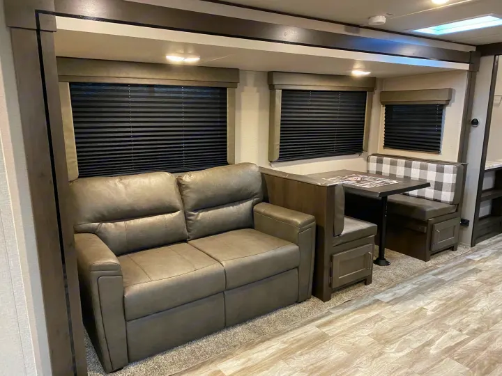 Inside an RV rental: a modern living space with a gray sofa, dining booth, and windows.. Grand Design Transcend Xplor 2022