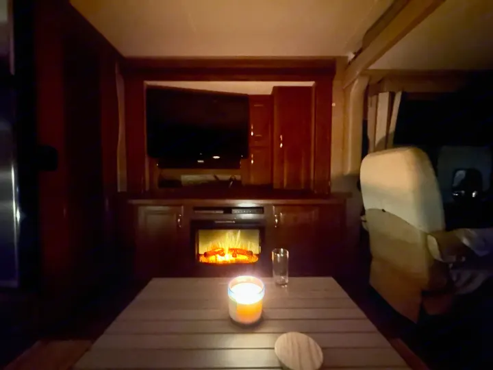 Cozy RV rental interior at night with an electric fireplace, TV, and candlelit table creating a warm ambiance.. Thor Challenger 2015