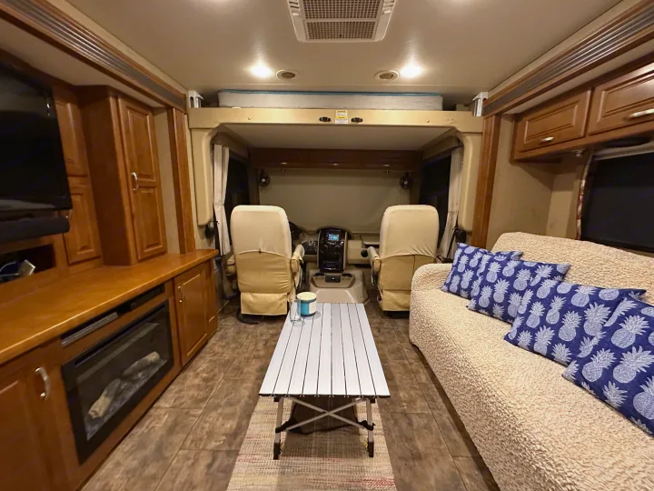 Spacious RV rental interior: cockpit, overhead bed, comfy sofa with pineapple pillows, table, and entertainment center.. Thor Challenger 2015
