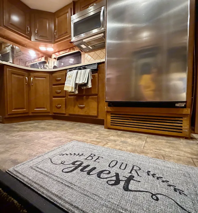 Spacious RV kitchen with wooden cabinets, stainless steel appliances, and a welcoming "BE OUR guest" mat, perfect for your next RV rental.. Thor Challenger 2015