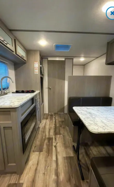 Spacious RV rental interior featuring a modern kitchen, dining area with marble-look table, and wood-look flooring for travel.. Other Other 2021