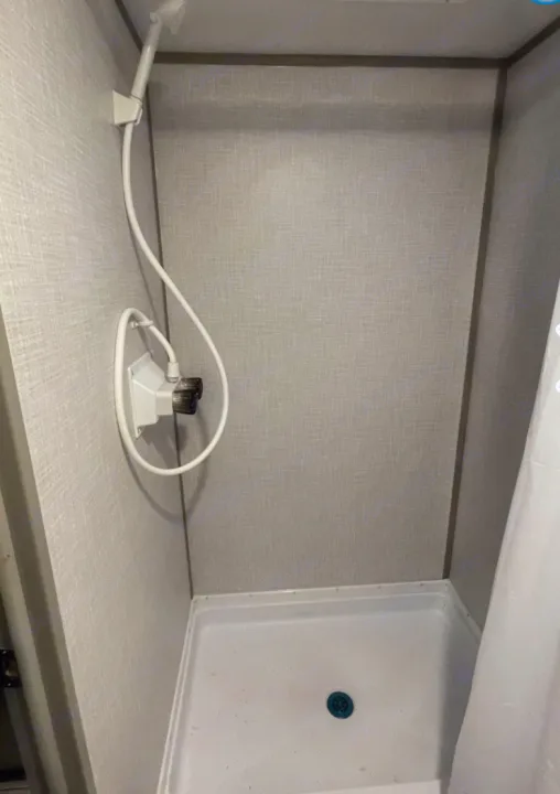 Compact RV rental shower with light walls, white base pan, blue drain, and handheld showerhead.. Other Other 2021