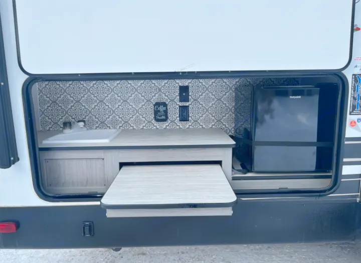 Explore this RV rental's outdoor kitchen! Features include a sink, Hotpoint mini-fridge, and convenient pull-out counter.. Heartland RVs Mallard 2021