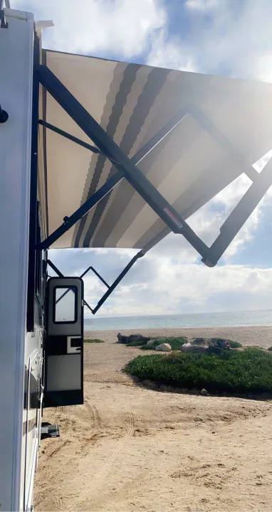Unforgettable rv rental experience: RV with open door & extended awning overlooking a sunny beach & ocean.. Coachmen Prism 2023