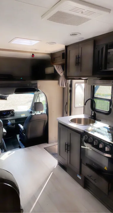 Spacious RV rental interior featuring a modern kitchen with sink and stove, light flooring, and driver's cabin.. Coachmen Prism 2023