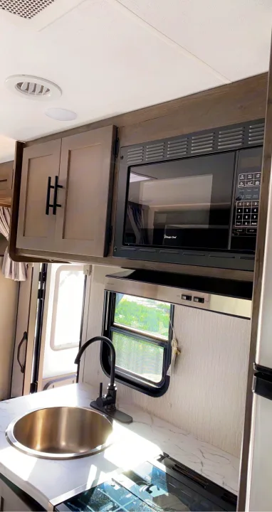 Modern RV rental kitchen with a sink, microwave, and cooktop, offering essential amenities for travelers.. Coachmen Prism 2023