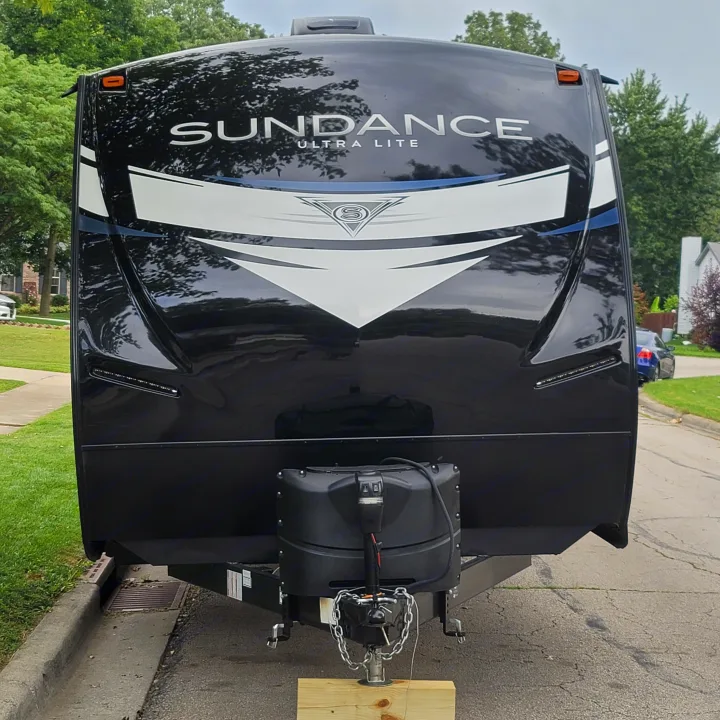 Front view of a black Sundance Ultra Lite RV rental, with hitch and propane tanks visible. Parked on asphalt beside grass.. Heartland RVs Sundance Ultra Lite 2022