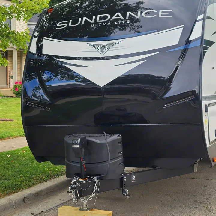 Front view of a black Sundance Ultra Lite travel trailer RV rental, showing the hitch and safety chains, parked on a street.. Heartland RVs Sundance Ultra Lite 2022