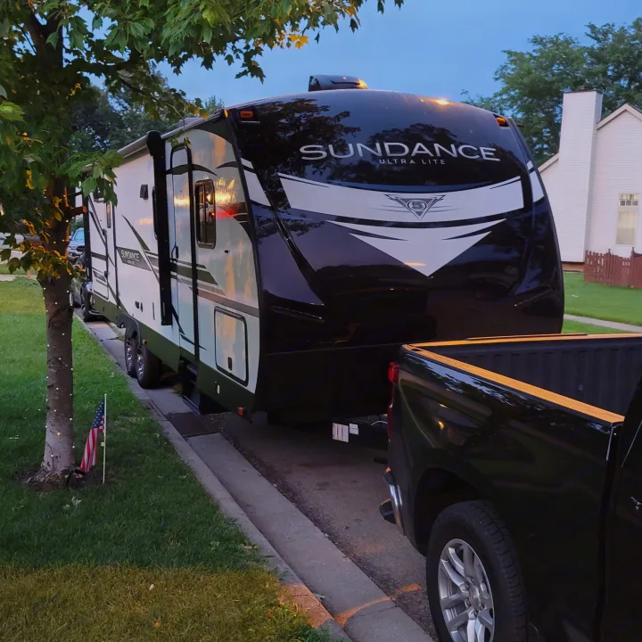 Black pickup truck towing a white & black 'Sundance Ultra Lite' RV rental on a residential street. Ready for travel.. Heartland RVs Sundance Ultra Lite 2022