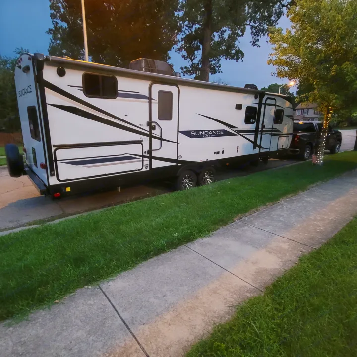 White Sundance Ultra Lite RV rental, a travel trailer, parked on a paved area next to a sidewalk and grass.. Heartland RVs Sundance Ultra Lite 2022