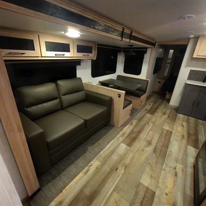 Inside a sleek **rv rental**: light wood-look flooring, a gray sofa, and built-in cabinetry create a modern living space.. Heartland RVs Sundance Ultra Lite 2022