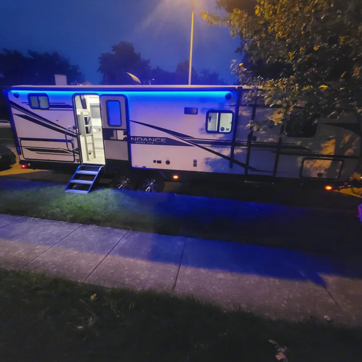 An RV rental glowing blue at night, parked with entry steps down.. Heartland RVs Sundance Ultra Lite 2022