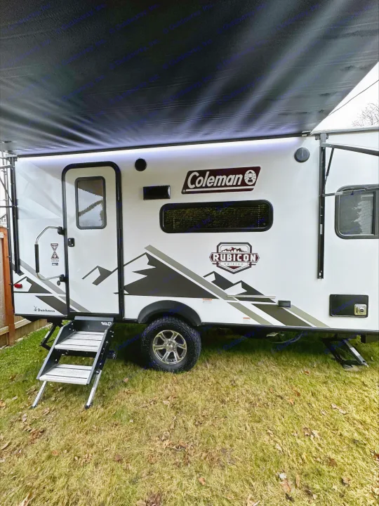 Coleman Rubicon travel trailer, ideal for your next RV rental adventure, parked on green grass with awning extended.. Dutchmen Coleman Rubicon 2021