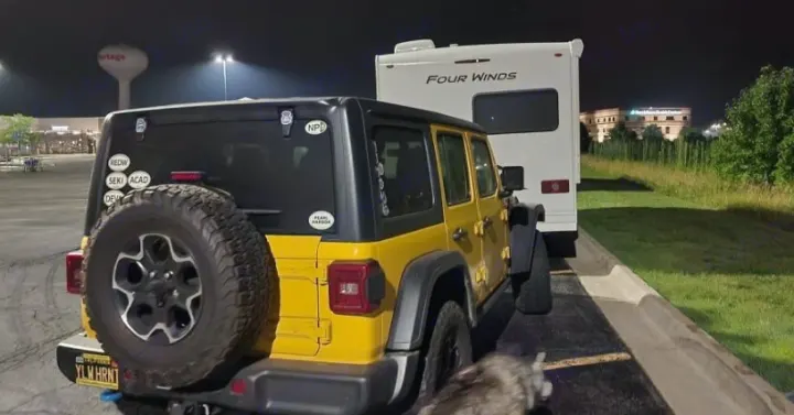 Yellow Jeep & Four Winds RV rental parked at night in a lit lot with a dog nearby. Perfect for cross-country travel.. Thor Four Winds 2022