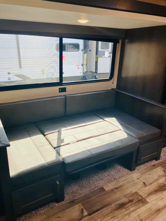 Sun-drenched RV rental interior. Features an L-shaped dinette/sofa with storage, ideal for travel trailer comfort.. Grand Design 265BH 2023