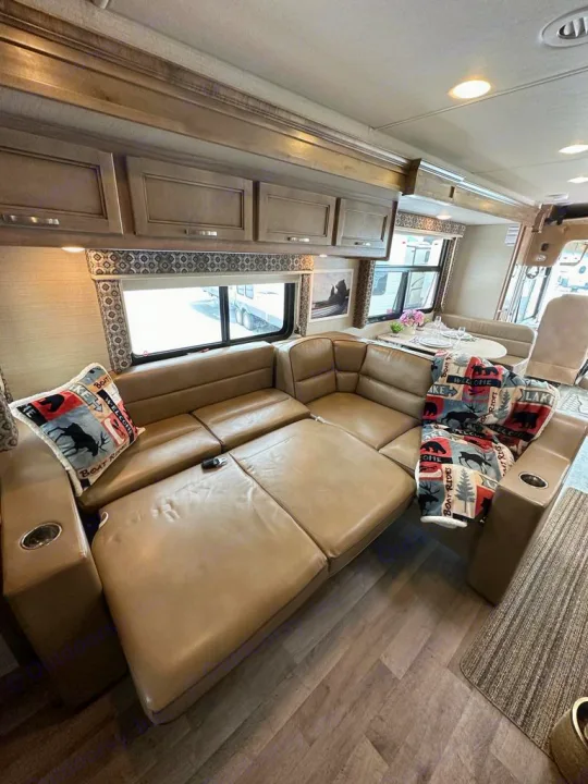 Inside a cozy RV rental: a long, light brown sectional sofa, dining table, and overhead storage cabinets create a comfortable living space.. Jayco Precept 2019
