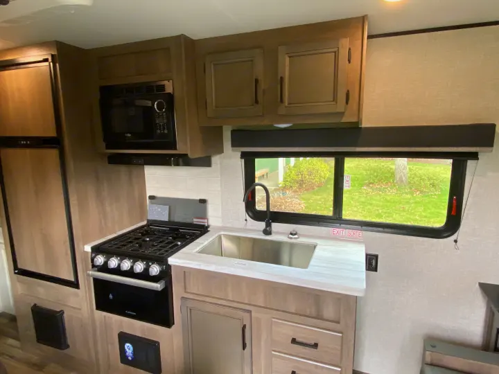Spacious RV rental kitchen with modern appliances: fridge, microwave, stove, and sink. Perfect for camper adventures.. StarCraft Autumn Ridge MB20 2023