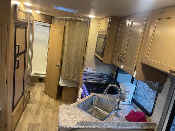 Compact RV rental interior features a kitchen with sink & stove, bathroom with shower, and a curtained sleeping area.. Thor Freedom Elite 2019