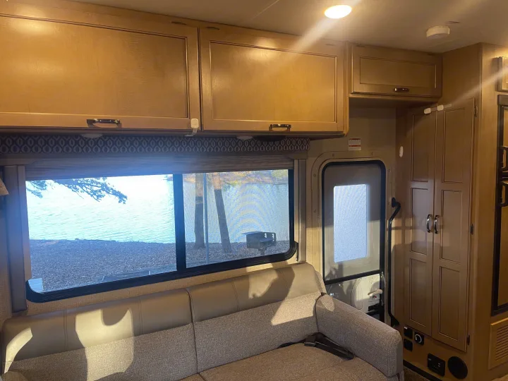Inside an RV rental: light wood cabinets, comfy sofa, and a serene lakeside view for your next adventure.. Thor Freedom Elite 2019
