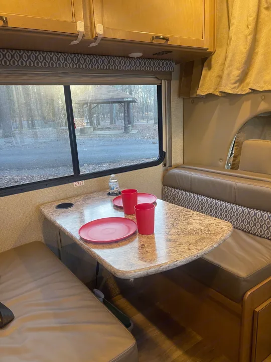 Inside this RV rental, a welcoming dinette with a table, benches, and plates, offering a peaceful camp view.. Thor Freedom Elite 2019