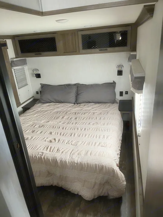 Cozy RV rental bedroom with a comfortable bed, nightstands, wall sconces, and overhead storage cabinets.. Forest River Sabre 2022