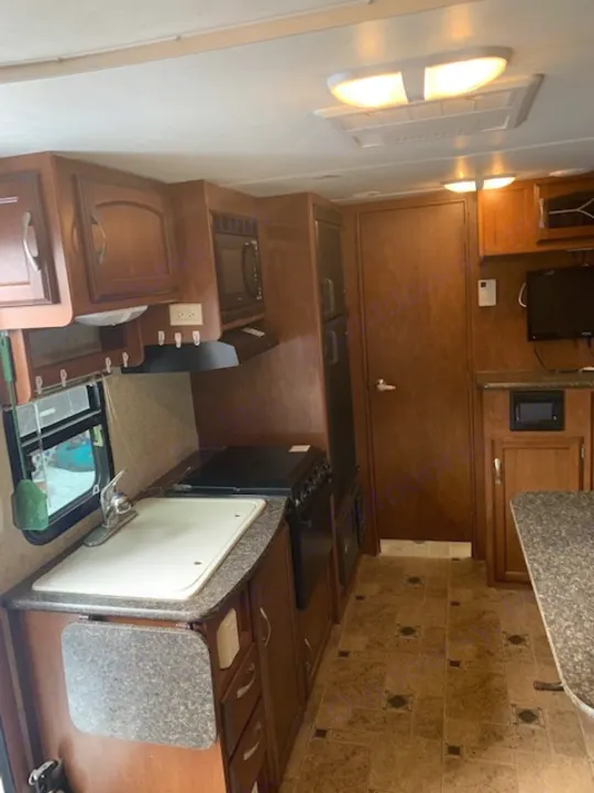 RV rental kitchen interior with wood cabinets, sink, stove, and microwave. Bright, functional space for your travels.. Winnebago Other 2013
