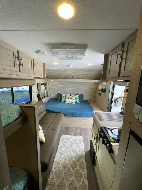 Bright RV rental interior showing a comfortable bedroom, bunk beds, kitchen, and seating area. Ideal for travel.. Forest River AURORA 2023